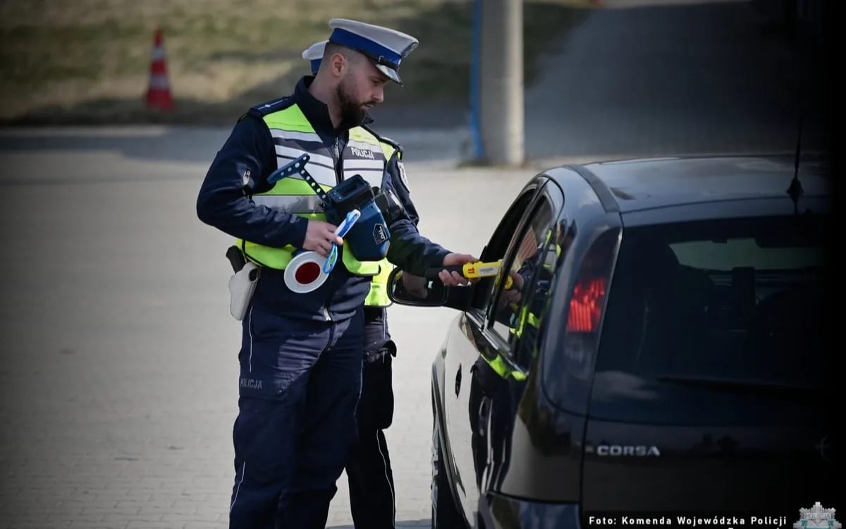 Policjant z alkomatem kontorluje kierowce samochodu osobowego